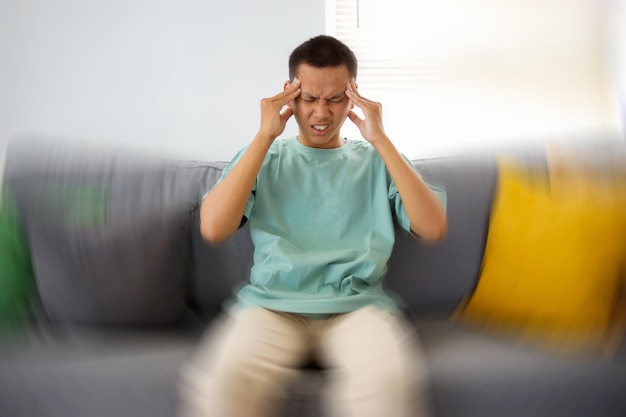 Photo young asian male feels dizzy while sitting on sofa with feeling pain and spinning sensation