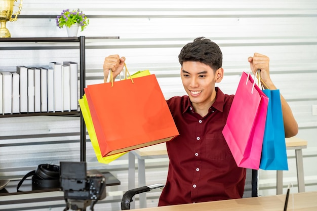 Young Asian male online merchant blogger using camera to live video show shopping bag with thumbup Social media and online Influencer concept