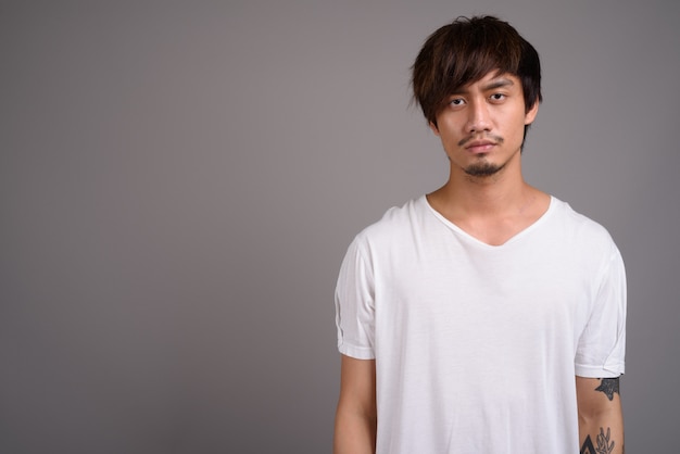 Young Asian man against gray wall