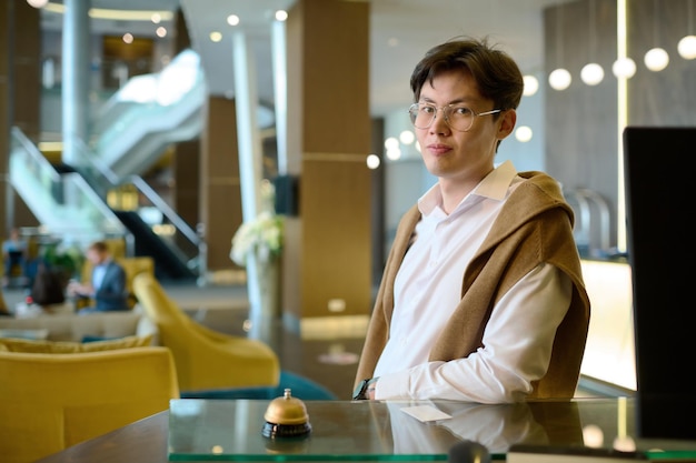 Young asian man in casualwear and eyeglasses waiting for receptionist by counter