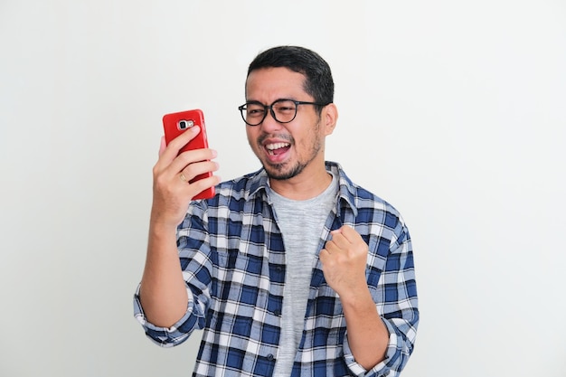 Young Asian man clenched fist to show excitement when looking to his handphone