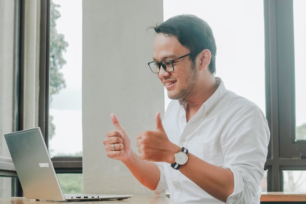 Young Asian man doing video conference on laptop computer while sitting at the cafe having meeting