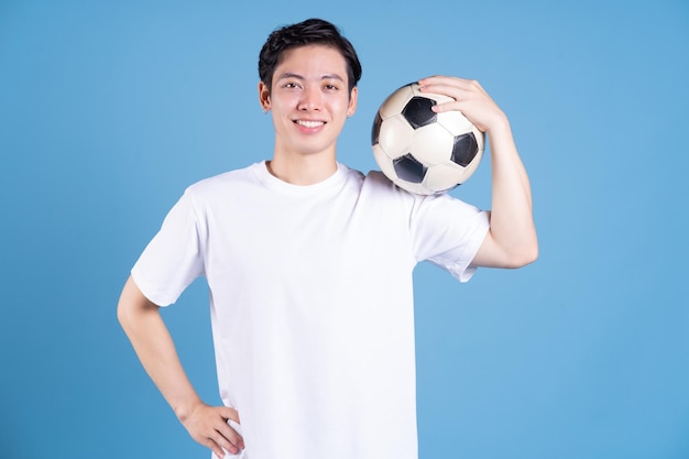 Young Asian man holding ball on background