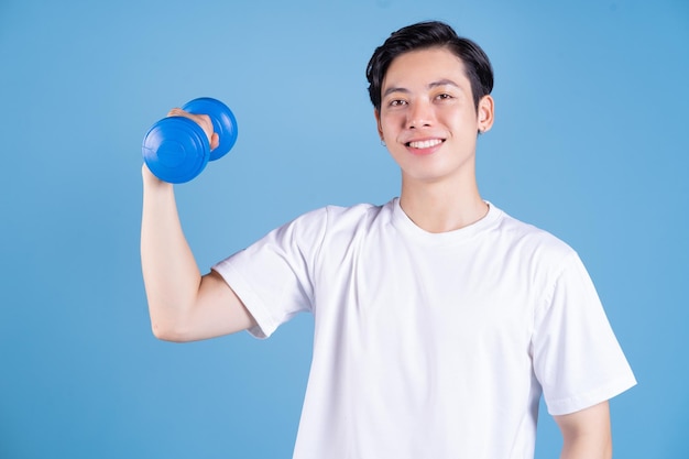 Young Asian man holding dumbbell on background