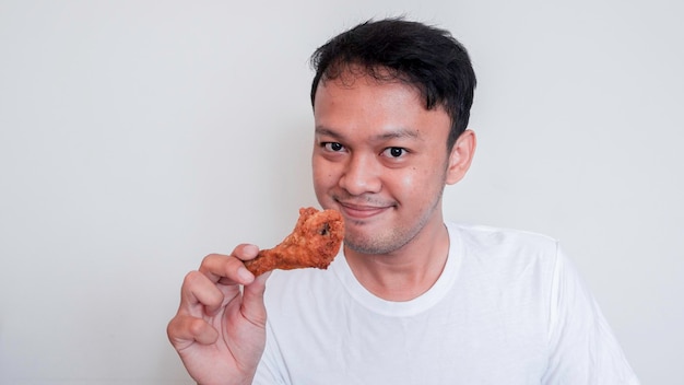 Young Asian man is eating fried chicken wear white shirt feeling happy and smile