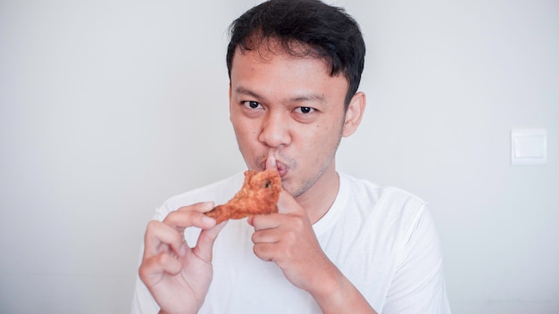 Young Asian man is eating fried chicken wear white shirt with silent hand gesture