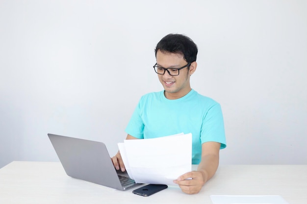 Young Asian Man is smile and happy when working on a laptop and document on hand Indonesian man wearing blue shirt