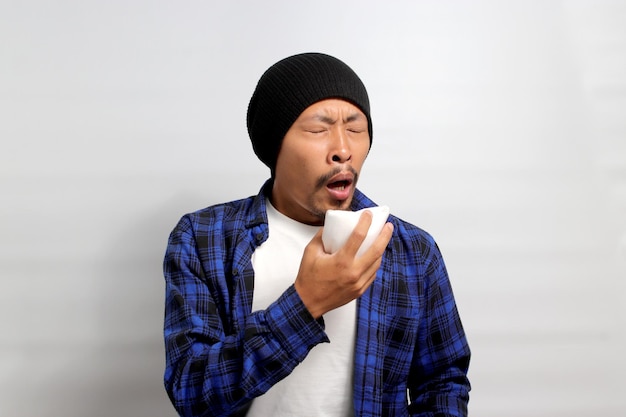 Young Asian man is sneezing and blowing his nose into a napkin due to the flu