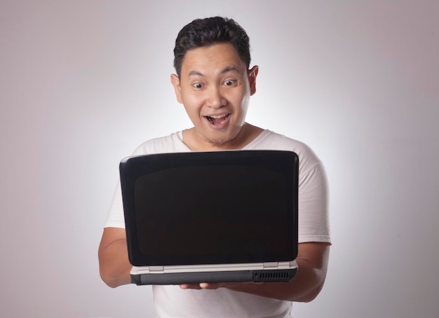 Young Asian man looking at laptop surprised expression Close up body portrait