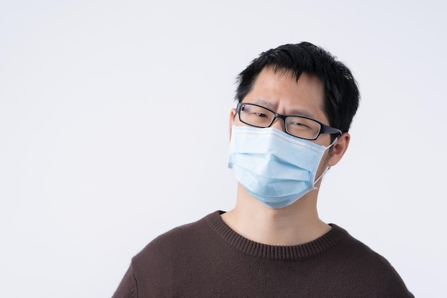 Young Asian man portrait feeling sick wearing a surgical blue face mask to prevent infection air pollution isolated on white background cut out