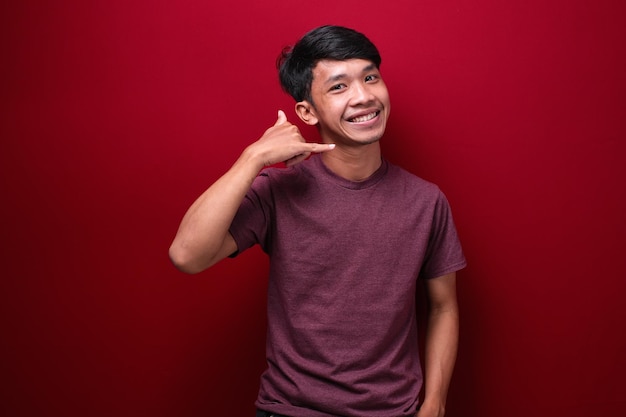 Young asian man red background smiling doing phone gesture with hand and fingers like talking on the telephone Communication concepts