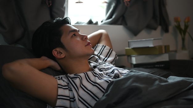 Young Asian man relaxing in his bed on weekend.