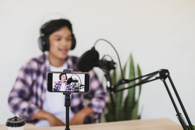 Young Asian man shooting video and recording podcast using smartphone and microphone on stand