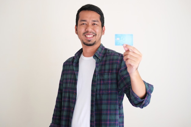 Young Asian man smiling confident while showing his blank credit card