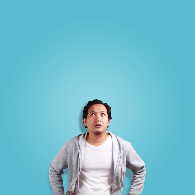 Young Asian man thinking expression eyes glance to the top over blue background with copy space