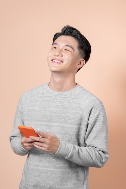 Young asian man using mobile phone isolated on beige background looking up while smiling