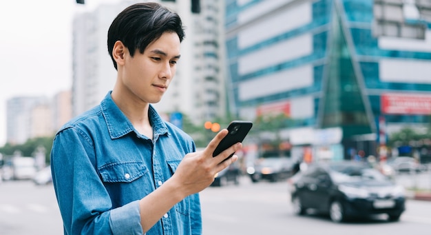 Young Asian man walking and using smartphone on the street