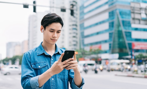 Young Asian man walking and using smartphone on the street