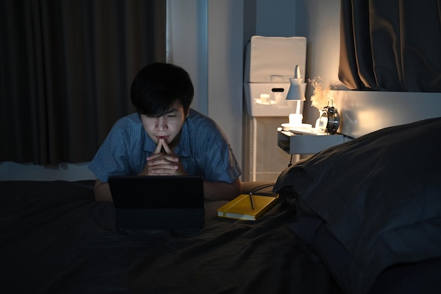 Young asian man watching movies on digital tablet at night