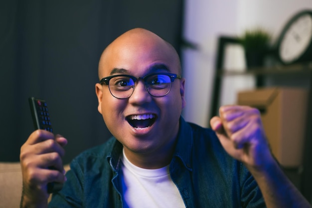 Young asian man watching television using remote to change the program