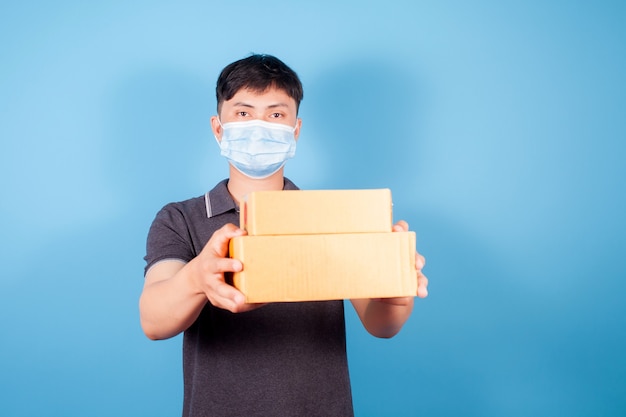 A young Asian man wearing a mask delivers express delivery boxes on blue background