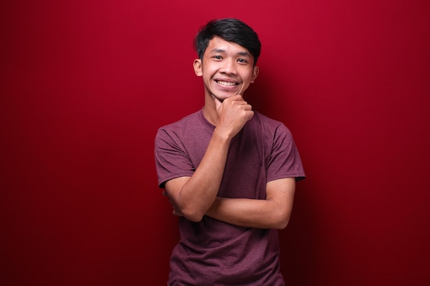 Young asian man wearing tshirt standing over red background Thinking worried about a question concerned and nervous with hand on chin