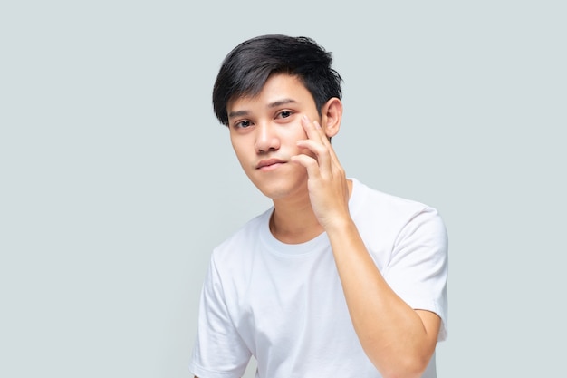 Young Asian man wearing a white Tshirt using his hand checking his face