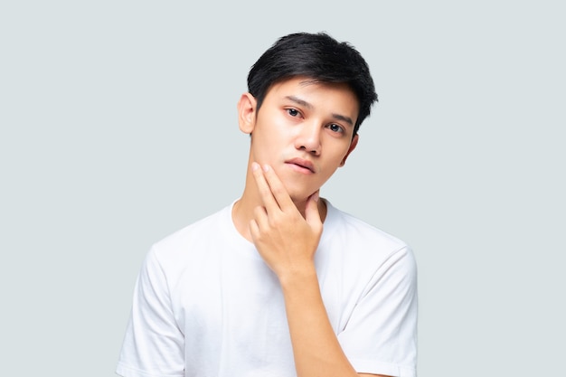 Young Asian man wearing a white Tshirt using his hand checking his face