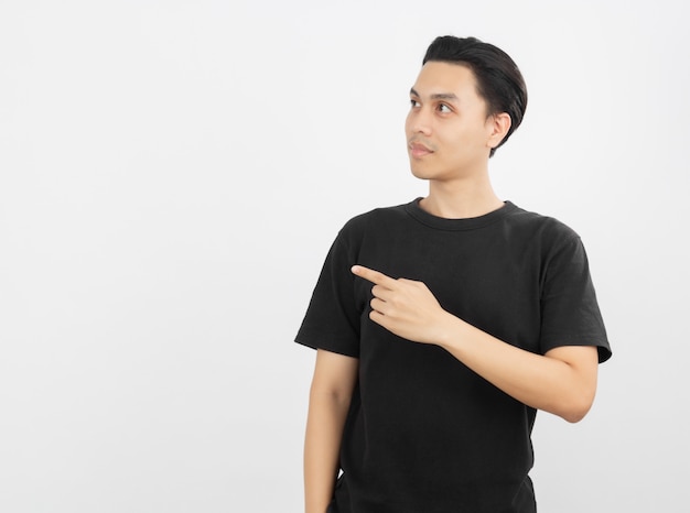 Young asian man with black shirt pointing to the side with a finger to present a product or an idea while looking forward surprising isolated on white