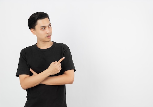 Young asian man with black shirt pointing to the side with a finger to present a product or an idea while looking forward surprising