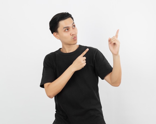 Young asian man with black shirt pointing to the side with a finger to present a product or an idea while looking forward surprising