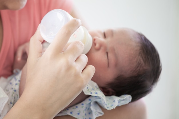 Young asian mother feeding her newborn baby girl with milk bottle