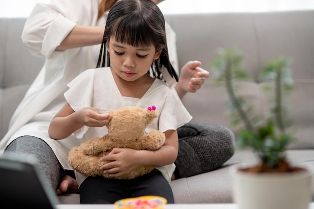 Young Asian mother tying daughter's hair