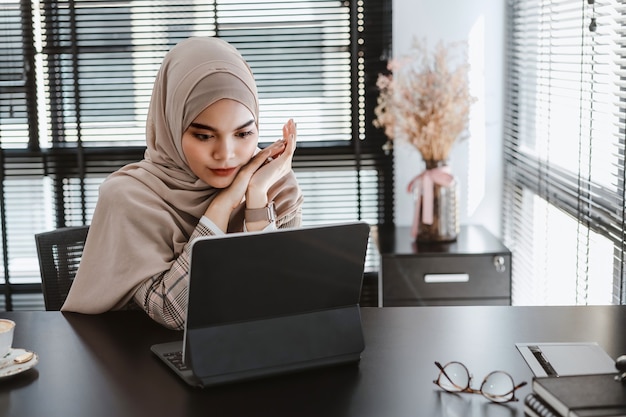 Young asian muslim business woman brown hijab sitting and working with laptop computer at modern office.