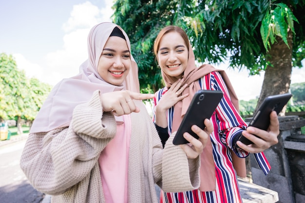 Young asian muslim woman in head scarf meet friends and using phone in the park