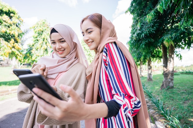 Young asian muslim woman in head scarf meet friends and using phone in the park