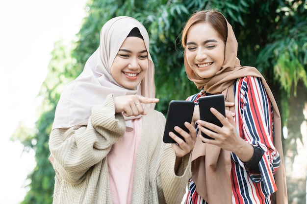 Young asian muslim woman in head scarf meet friends and using phone in the park