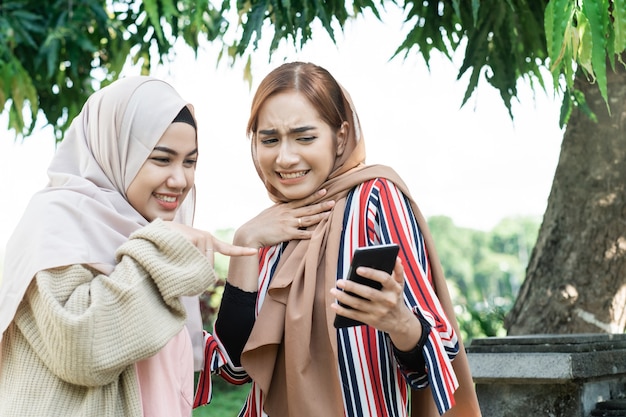 Young asian muslim woman in head scarf meet friends and using phone in the park