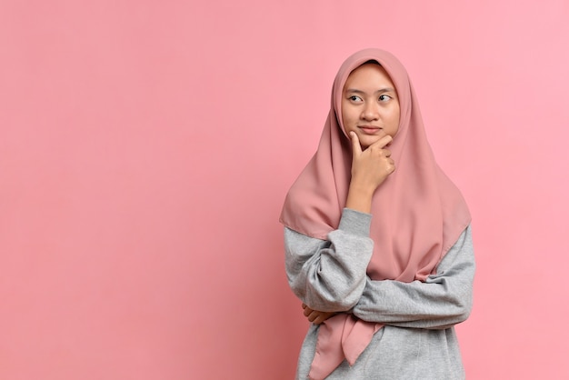 Young Asian muslim woman looking at a copy space or thinking an idea; isolated in pink background