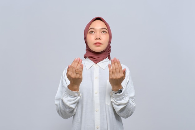 Young Asian Muslim woman raising hands and praying to god isolated over white background