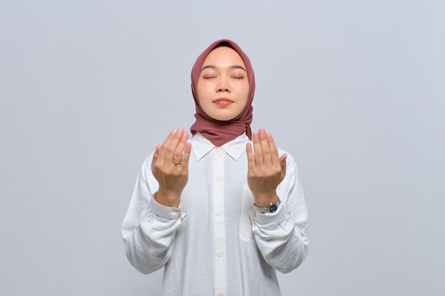 Young Asian Muslim woman raising hands and praying to god isolated over white background