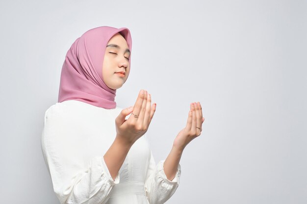 Young Asian Muslim woman raising hands and praying to god isolated over white background