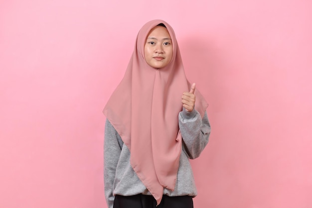 Young Asian Muslim woman showing thumb up against pink colour background Mock up copy space Showing thumb up