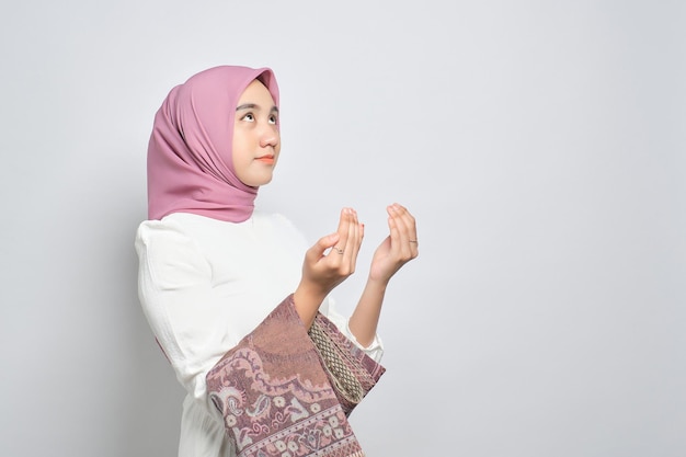 Young Asian Muslim woman with prayer mat raising hands and praying to god isolated over white background