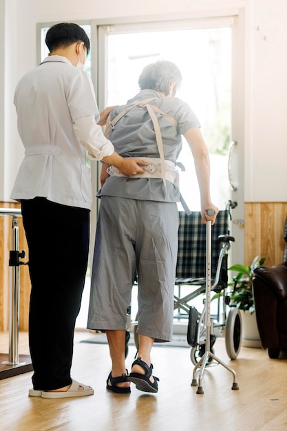 Young asian physical therapist working with old man on working using a walker in hallway of nursing home