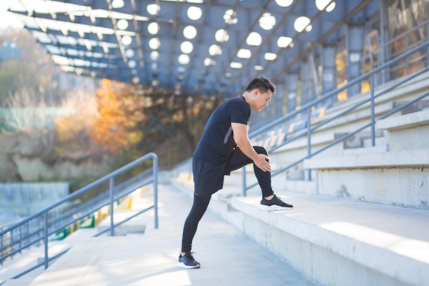 Young asian runner athlete with muscle pain. Man massaging Stretching, trauma injury while jogging at the stadium outdoors. Fitness male sprain severe pain stretch pull. Leg muscle cramp calf sport