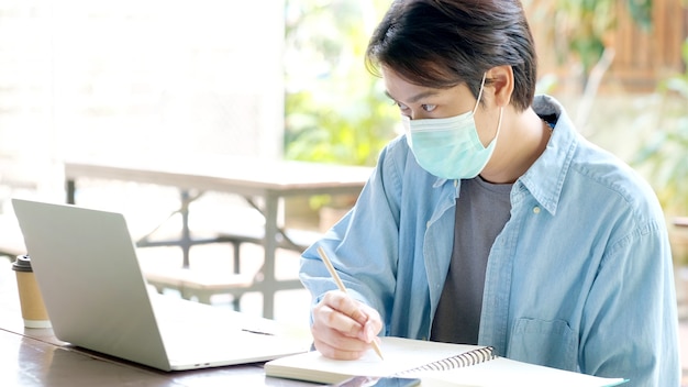 Young asian student man wearing protection mask working with laptop