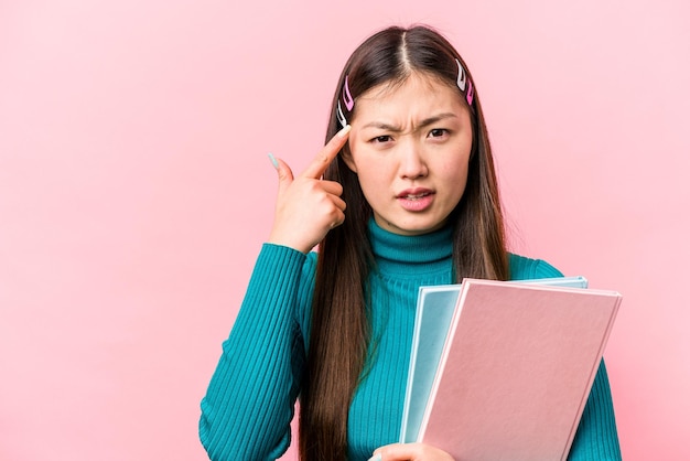 Young asian student woman holding books isolated on pink background showing a disappointment gesture with forefinger