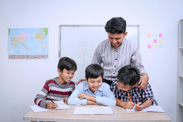 Young Asian teacher and happy elementary multiethnic students reading a book together in the classro