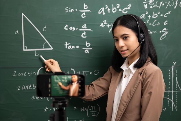 Young asian teacher woman standing looking at camera and video conference with student Female teacher training the mathematics in classroom from live stream with smartphone online course